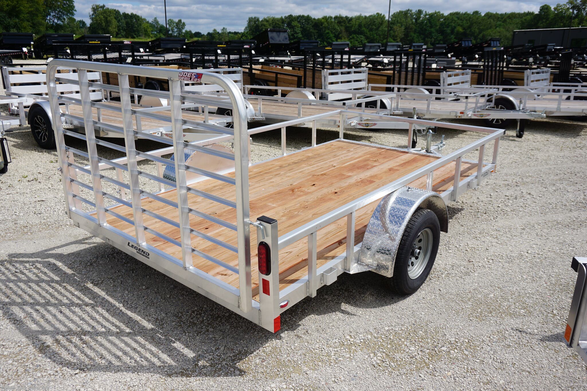 Legend 7x12 Open Deluxe Utility Trailer, 17" deck height utility trailer, 48" ramp gate trailer, 3.5k EZ-Lube spring axle, ST205/75R14 Silver Mod steel tires, 3" tube cross members, 24" on center cross member spacing, 4" tube frame trailer, aluminum flooring utility trailer, LED lighting trailer, 2" straight coupler, 2k top-wind jack, ATP fenders, stake pockets, aluminum utility trailer, open deluxe trailer, Legend utility trailer, lightweight utility trailer, durable trailer frame, trailer with LED lights, easy-to-lube axle, high-quality utility trailer, trailer with ramp gate, spring axle utility trailer, Legend trailer features, utility trailer with aluminum flooring, adjustable coupler trailer, top-wind jack utility trailer, trailer with ATP fenders, customizable utility trailer, Legend open trailer, utility trailer for heavy loads, trailer for equipment transport, low-profile utility trailer, trailer with stake pockets, utility trailer for landscaping, 12' utility trailer, trailer